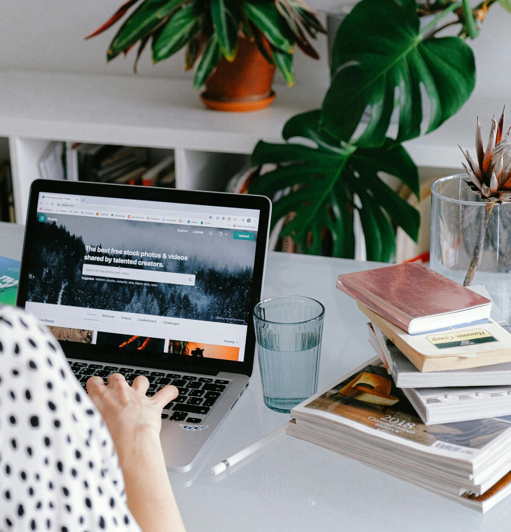 A woman working from home on her laptop surrounded by plants and books for a cozy office feel.